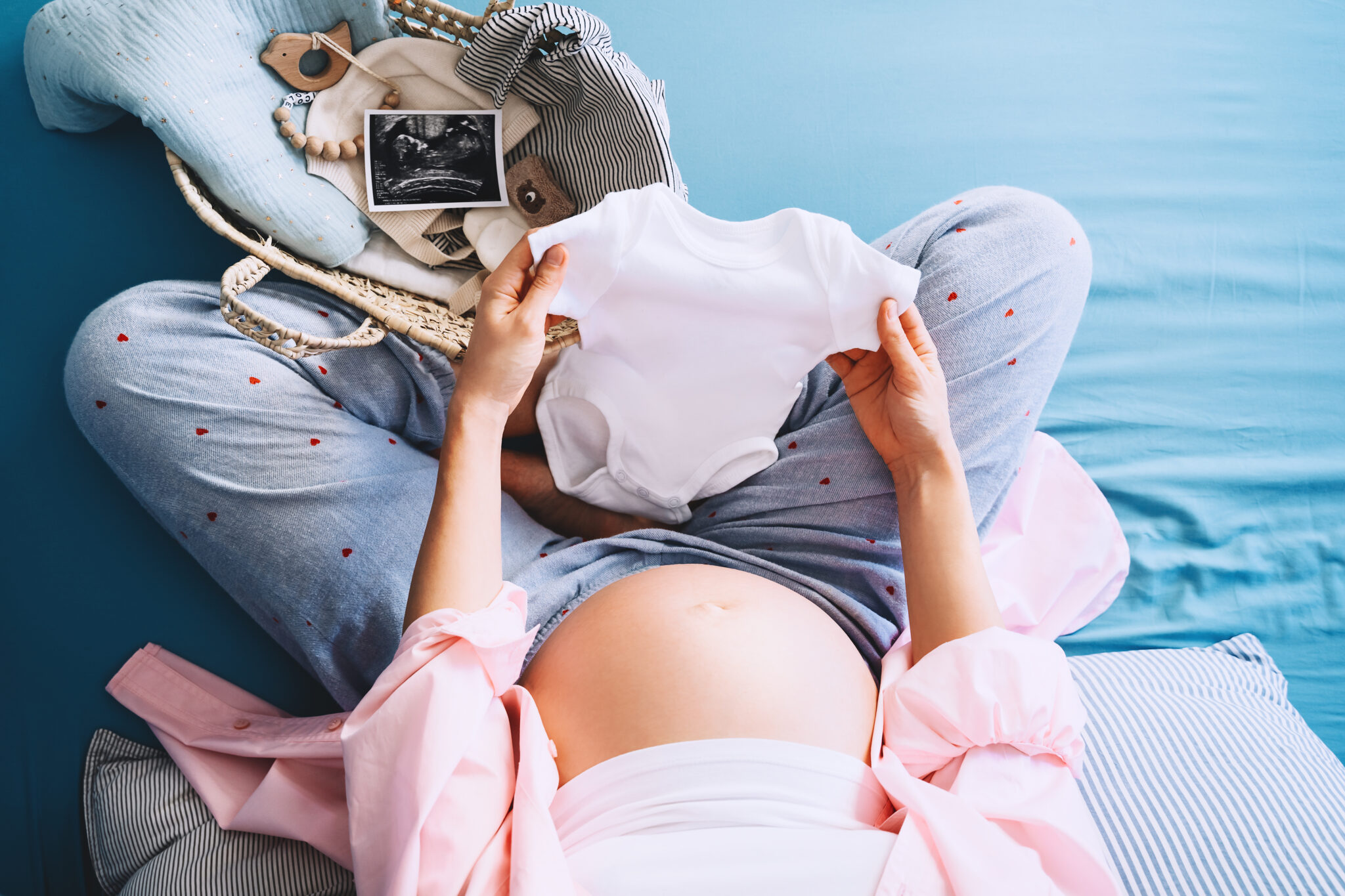 Pregnant woman holding baby bodysuit preparing to child birth du